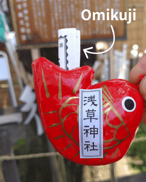 A paper fortune tucked into a cute red fish (Tai) figure from Asakusa Shrine.